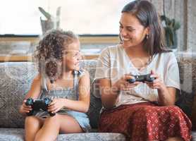 Hispanic mother and daughter playing video games together while sitting on the couch at home. Fun young mother and daughter using joysticks while playing and spending free time together on weekend