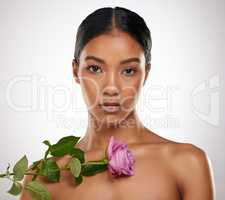 Embrace your femininity. Studio portrait of an attractive young woman posing with a pink rose against a grey background.