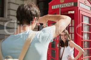 Youre officially in London when you see one of these. Shot of a young man taking photos of his girlfriend with smartphone in a telephone booth while exploring the city of London.