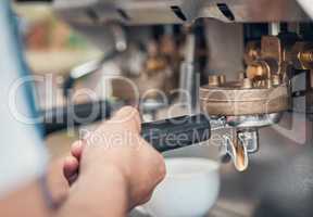 Closeup of a barista using a portafilter while preparing ground coffee to make a shot of espresso for cappuccino or latte in a cafe. Hands of waiter using a brewing machine to make a warm beverage in a coffeeshop