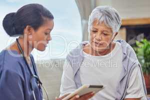 A hispanic senior woman in on a cosy sofa and her female nurse in the old age home and using a digital tablet. Mixed race young nurse and her patient talking in the lounge