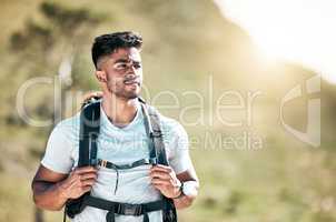 Athletic young mixed race man wearing a backpack taking a break during a hike. Fit handsome hispanic man standing outside and looking at the view while hiking outside in nature. An outdoor workout