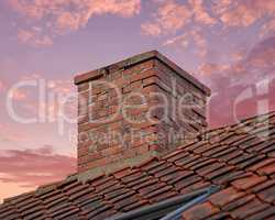 Closeup of red brick chimney against a colorful sunset sky for combustion gases and home insulation on tiled roof. Architecture design on house building for smoke extraction from fireplace or furnace