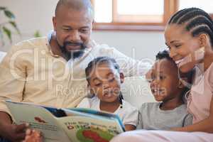 A young african american family sitting on the sofa together and smiling while reading a story book at home