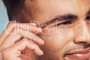 Closeup of one handsome young indian man using a tweezer to remove hair from his eyebrows. Face of a mixed race guy using beauty tool in his skincare treatment routine. Hand of a man holding a tweezer grooming himself