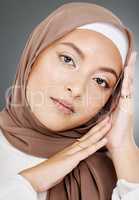 Portrait of a glowing elegant muslim womans face isolated against grey studio background. Young woman wearing a hijab or headscarf, showing her eyelash extensions, jewellery and skin routine