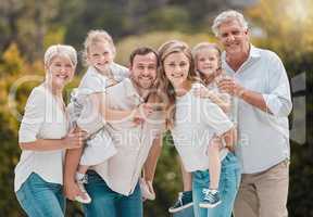 Portrait of a smiling multi generation caucasian family standing close together in the garden at home. Happy adorable girls bonding with their mother, father, grandfather and grandmother in a backyar