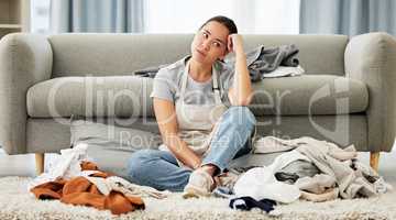 A young mixed race domestic cleaner looking distracted and overwhelmed while folding laundry. A beautiful Asian woman daydreaming while doing household chores in her apartment