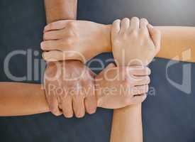 Closeup of diverse group of people from above holding each others wrists in a circle to express unity, support and solidarity. Connected hands of multiracial community linked for teamwork in a huddle. Society join together for collaboration and equality