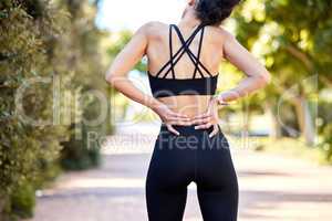 One mixed race woman from behind holding sore lower back while exercising outdoors. Female athlete suffering with painful spine injury from fractured joint and inflamed muscles during workout. Struggling with stiff body cramps causing discomfort
