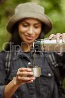 Coffee break. an attractive young woman drinking some coffee while hiking in the wilderness.