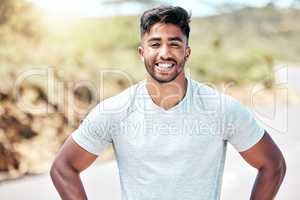 Portrait of happy young mixed race man getting ready to workout. Young hispanic man smiling and standing with his hands on his hips outside. Getting fitter with each day of running and exercise