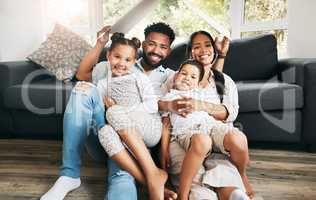 Portrait of a hispanic family holding a cardboard shaped roof at home. Mixed race family covered by a cardboard roof at in the lounge while sitting on the floor
