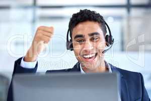 One happy young mixed race male call centre telemarketing agent cheering with joy and punching the air with fist while working in an office. Excited business man celebrating successful achievement in sales and reaching targets to win