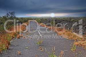Empty road through a field with burnt grass and cloudy sky with copy space. A curved countryside road or open asphalt roadway between dry land near Mauna Kea volcanic mountainside, Hawaii, Big Island