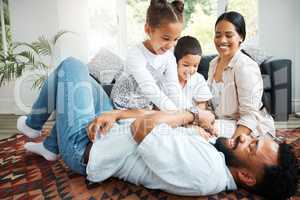 Closeup of a young hispanic family playing together on the lounge floor at home. Mixed race father and mother having fun while playing with their cute little son and daughter in the lounge at home