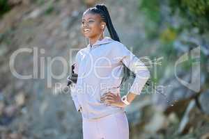 Young happy african american woman hiking on a mountain, taking a break to rest. Black ethnic fit smiling young woman working out in nature. Athletic woman standing on a hiking trail relaxing while listening to music on her earphones outside and enjoying 
