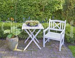 White wooden chair and table in a green garden with blossoming plants and copyspace. Tranquil landscape to relax and enjoy a cosy picnic in summertime. Outdoor patio in a quiet and secluded courtyard