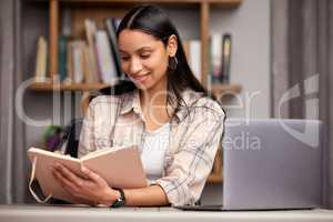 Finals are gonna be a breeze. an attractive young female student taking notes while studying in the library using her laptop.