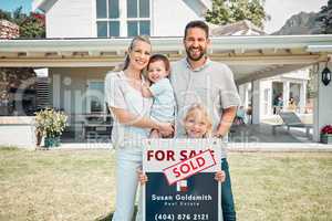 Portrait of happy caucasian family holding for sale and sold sign while relocating and moving in new house. Smiling parents and kids securing homeowner loan for property real estate and home purchase