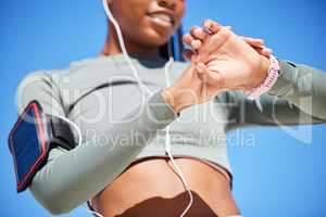 Fit african american woman checking her smartwatch, timing her progress. Athletic woman listening to music on her cellphone with earphones, checking her pulse on her watch while exercising outside