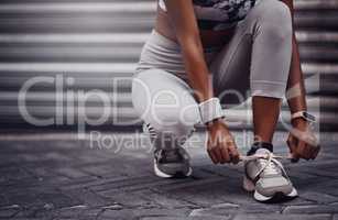 Closeup of one mixed race woman tying her shoelaces while exercising outdoors. Athlete fastening sneaker footwear for a comfortable fit and to prevent tripping while getting ready for cardio training workout or run in the city