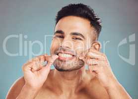 Portrait of one smiling young indian man flossing his teeth against a blue studio background. Handsome guy grooming and cleaning his mouth for better oral and dental hygiene. Floss daily to prevent tooth decay and gum disease
