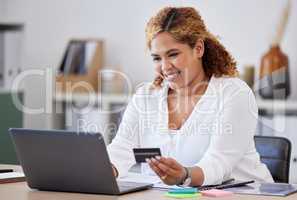 Happy businesswoman holding and using a credit card and typing on a laptop alone at work. One content hispanic female businessperson making an online purchase with her debit card and laptop