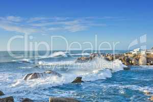 A rocky coastline in the Cape Province, South Africa. Ocean waves crashing on coastal rocks on a sunny summer day with blue clear skies and a scenic tropical landscape beachfront in the Western Cape