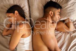 We spend more time fighting than in love. High angle shot of a young couple lying in bed with their backs to each other after an argument.