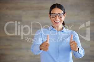 Smiling businesswoman showing thumbs up sign with copyspace. Mixed race professional standing alone and using hand gestures to symbol good luck. Hispanic woman wearing glasses endorsing and supporting