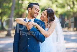 Happy romantic couple standing together on their wedding day. Bride embracing her groom from behind as they gaze into each others eyes. Newlyweds posing together in nature