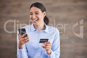 Young mixed race happy businesswoman using a credit card and phone to shop online at work. One hispanic woman paying for a purchase using her phone. Woman buying products using her phone and bank card