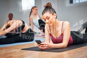 Take taking a quick breather. Shot of a young woman using her smartphone during a yoga lesson.