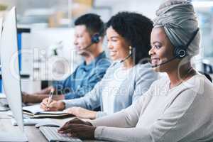 African american female call centre telemarketing agent working on computer alongside colleagues in an office. Group of diverse consultants troubleshooting solution for customer service and sales support