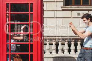 London called, we answered. a young man taking photos of his girlfriend with smartphone in a telephone booth while exploring the city of London.