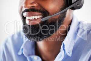 Closeup of one happy african american call centre telemarketing agent with big smile talking on headset while working in office. Face of confident friendly businessman operating helpdesk for customer service and sales support