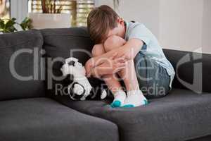 A soft toy is God to an unhappy child. Shot of a little boy comforting himself on a sofa at home.