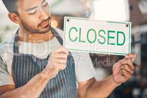 One young hispanic man holding a closed sign at a window on display in a store. Mixed race guy showing the closure of his small business or shop due to bankruptcy and recession