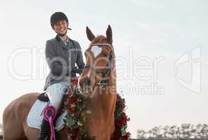 We won. a young female jockey sitting on her wreath-wearing horse after winning a race.