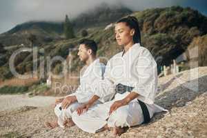 Keep calm and train on. two young martial artists meditating while practicing karate on the beach.