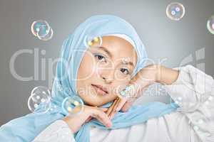 Portrait of a beautiful muslim woman wearing blue hijab headscarf against grey background. Arab female in a happy daydream and fantasy surrounded by the pure delight and innocence of playful bubbles