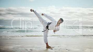 Kicking into gear. Full length shot of a handsome young male martial artist practicing karate on the beach.