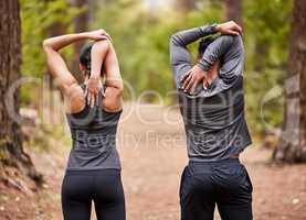 Rear view of young male and female athlete stretching before a run outside in nature. Two fit sportspeople doing warm-up exercises in pine forest on a sunny day