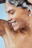 Freshening up all over. Studio shot of an attractive young woman washing her hair while taking a shower against a blue background.