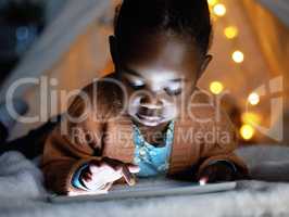 A small device packed with big life lessons. an adorable little girl using a digital tablet during bedtime at home.