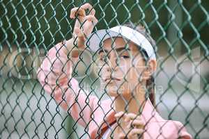 Close up of a female athlete leaning against a wire fence. Young hispanic tennis player posing on a tennis court wearing a white visor and pink jacket