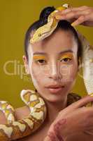 Trust is a strong word. Shot of a young woman posing with a snake around her neck against a yellow background.