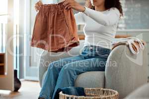 Woman folding a pair of shorts. Woman relaxing at home cleaning clothing. Woman sitting in a chair folding laundry. Woman doing housework chores at home cropped. Mixed race woman folding neat clothing