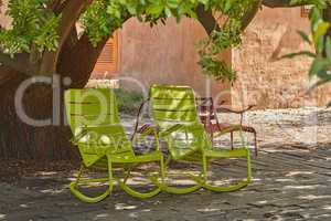 Two green vintage courtyard rocking chairs under a shady tree in a secluded and private garden at home. Patio furniture and seating set to enjoy and relax in summer. Lounging and feeling cosy outside